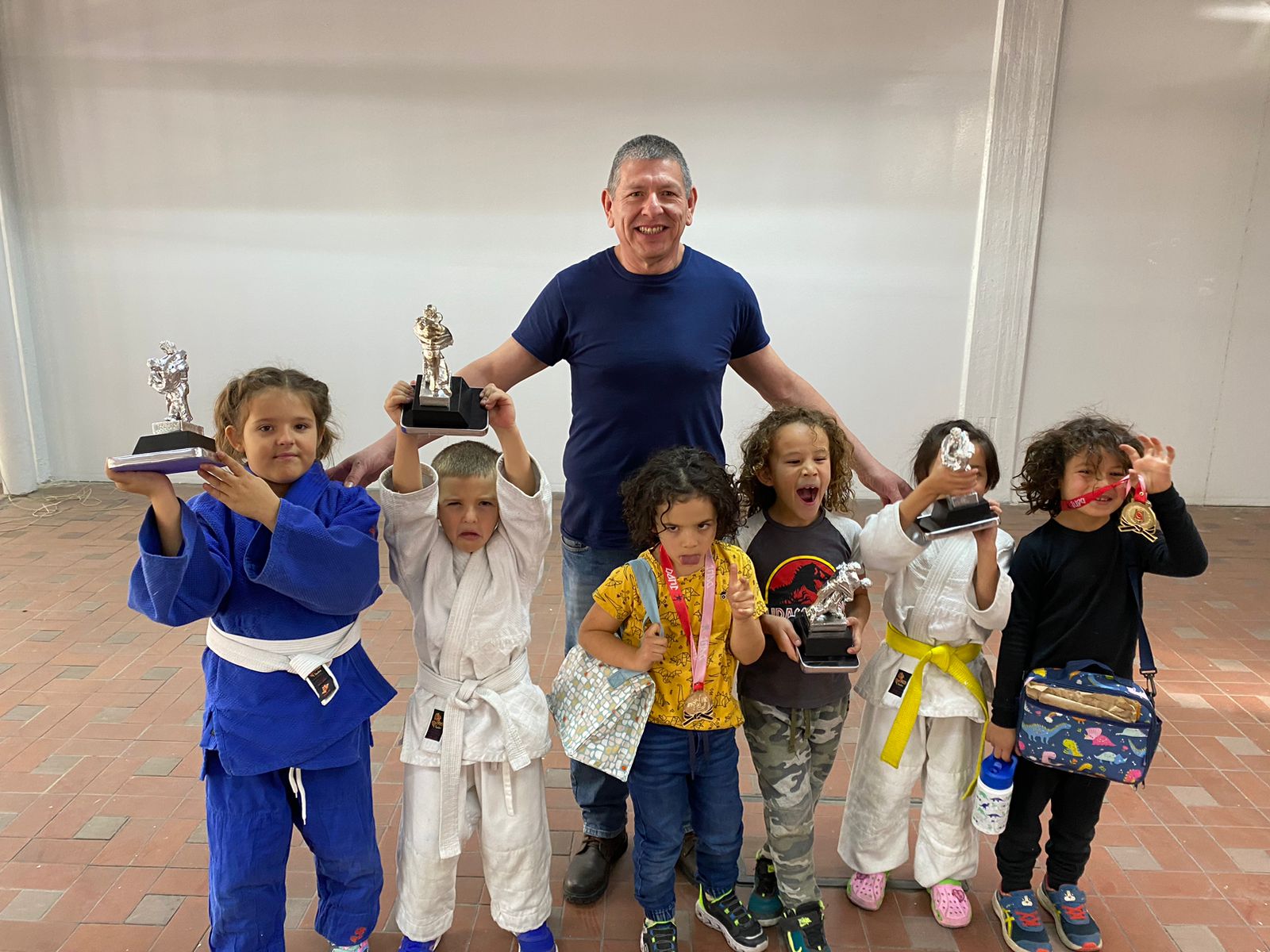 Niños del Club de Judo ERA celebrando con trofeos junto a su sensei