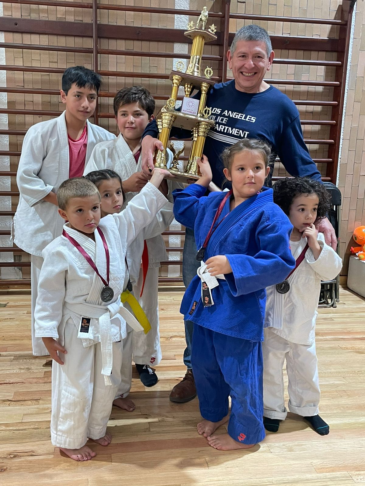 El Prof. Erick Ruiz Arteaga con sus alumnos infantiles y un trofeo ganado en una competencia de judo en CDMX